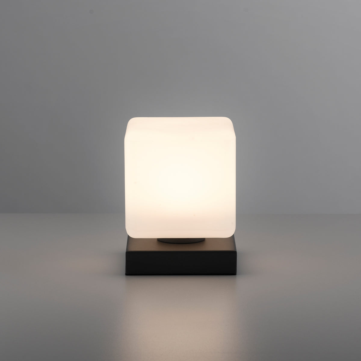 Lampe allumée de face sur fond gris, diffusant une lumière chaude.