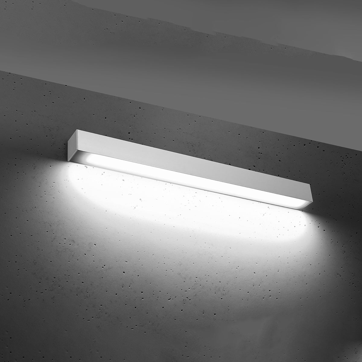 Luminaire allumé projetant un large halo lumineux blanc sur le mur