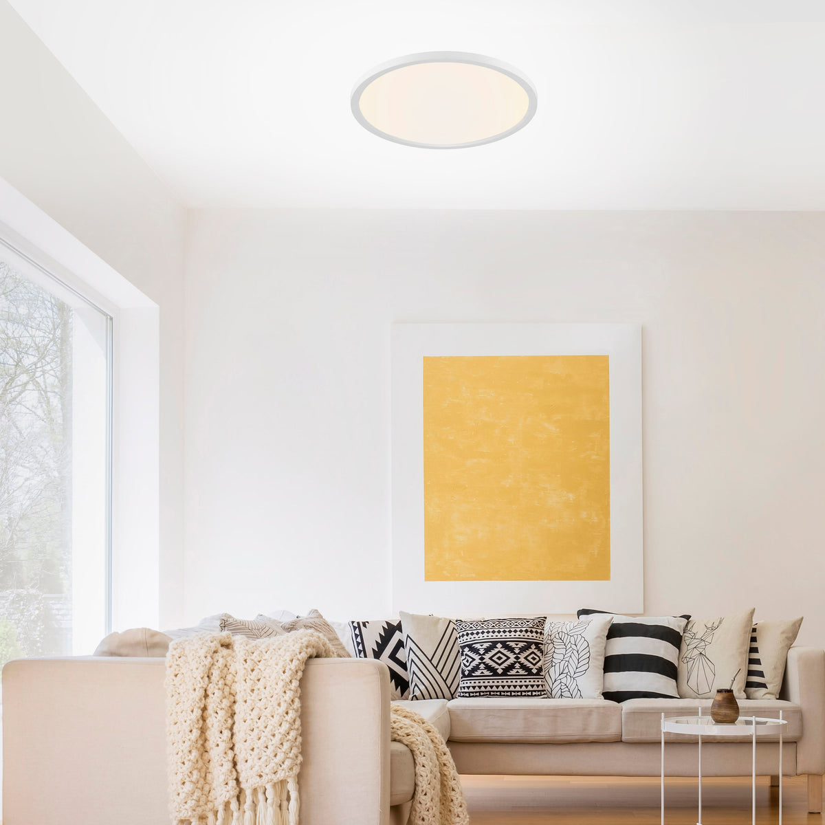 Mise en ambiance du plafonnier allumé au plafond d'un salon blanc avec canapé beige.