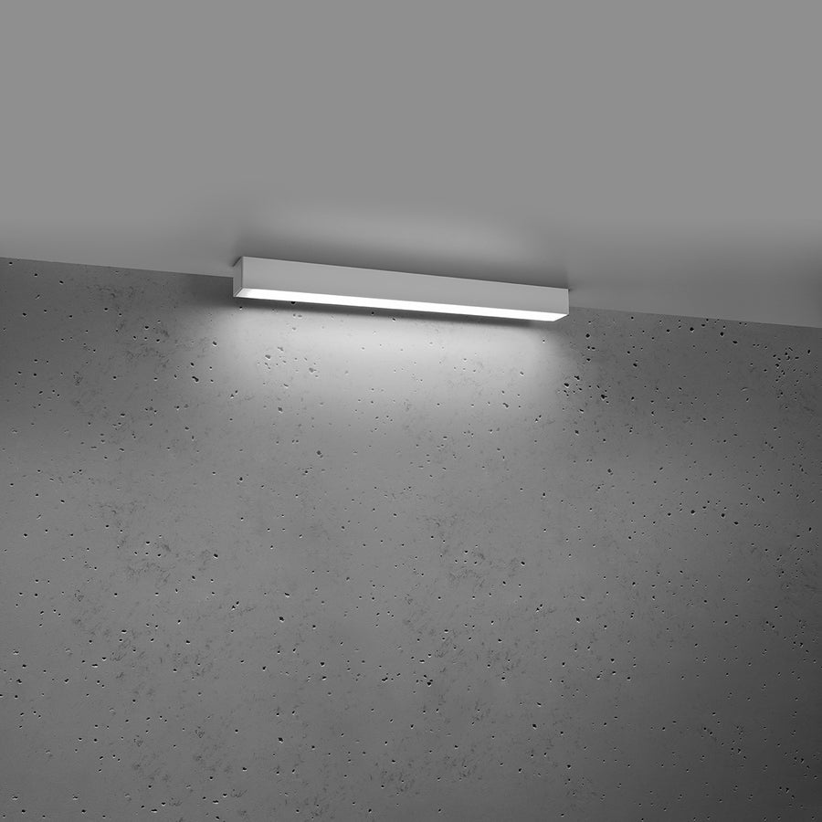 Le luminaire allumé projette un halo blanc diffus sur le mur gris.