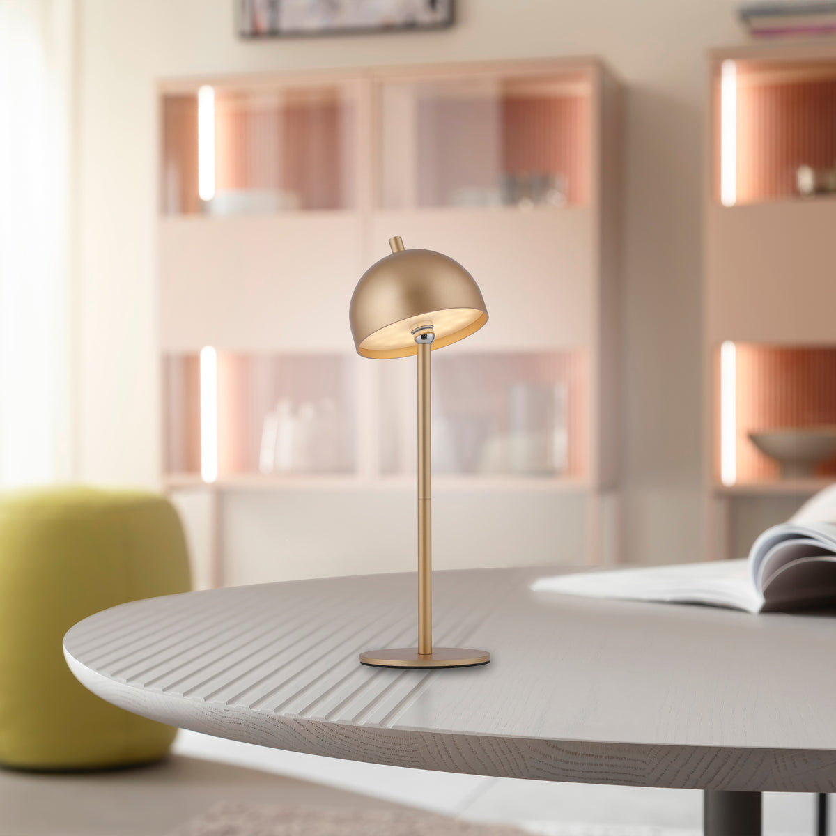 Mise en ambiance sur table en bois clair, bibliothèque rose et fauteuil vert en arrière-plan