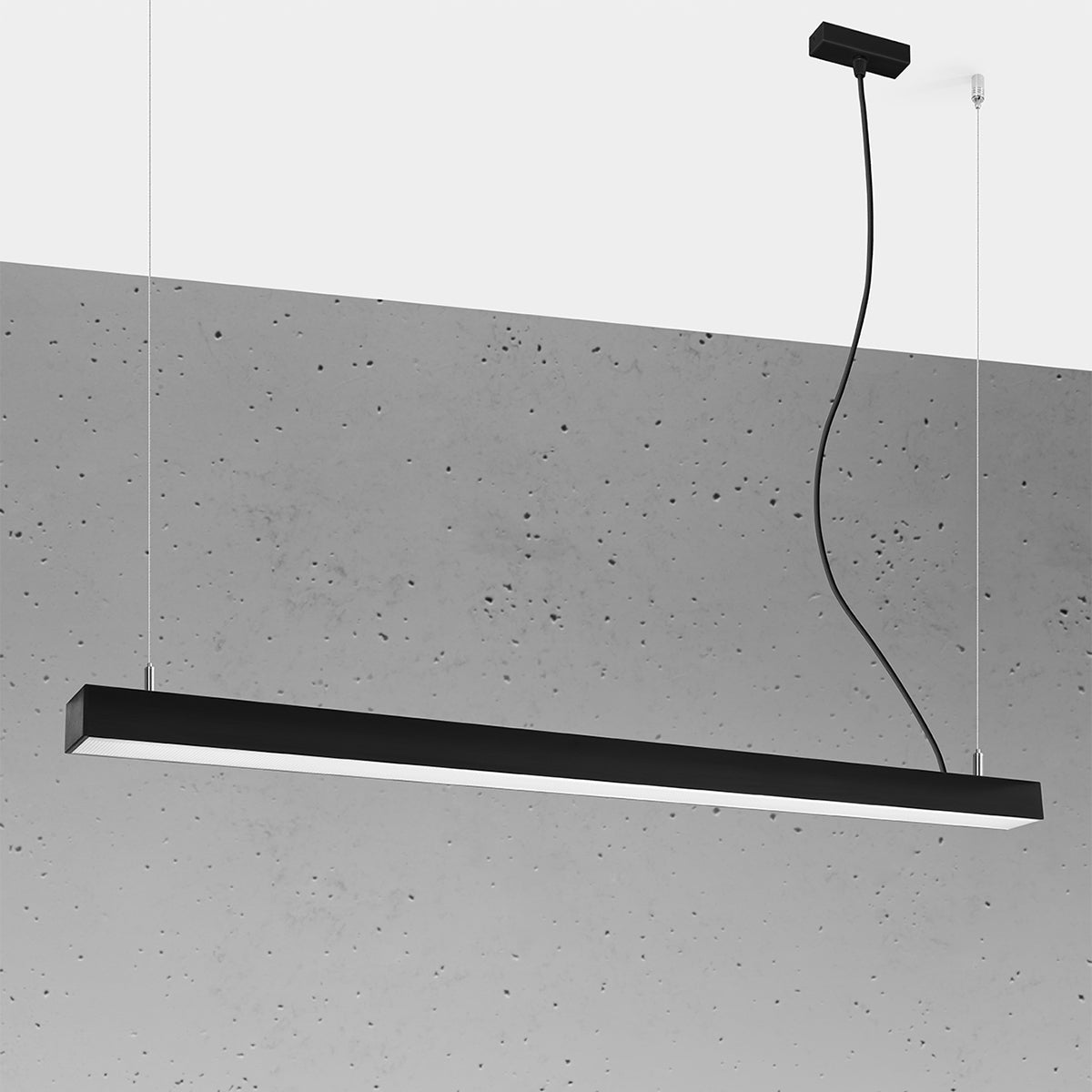 Luminaire suspendu linéaire allumé devant un mur en béton brut