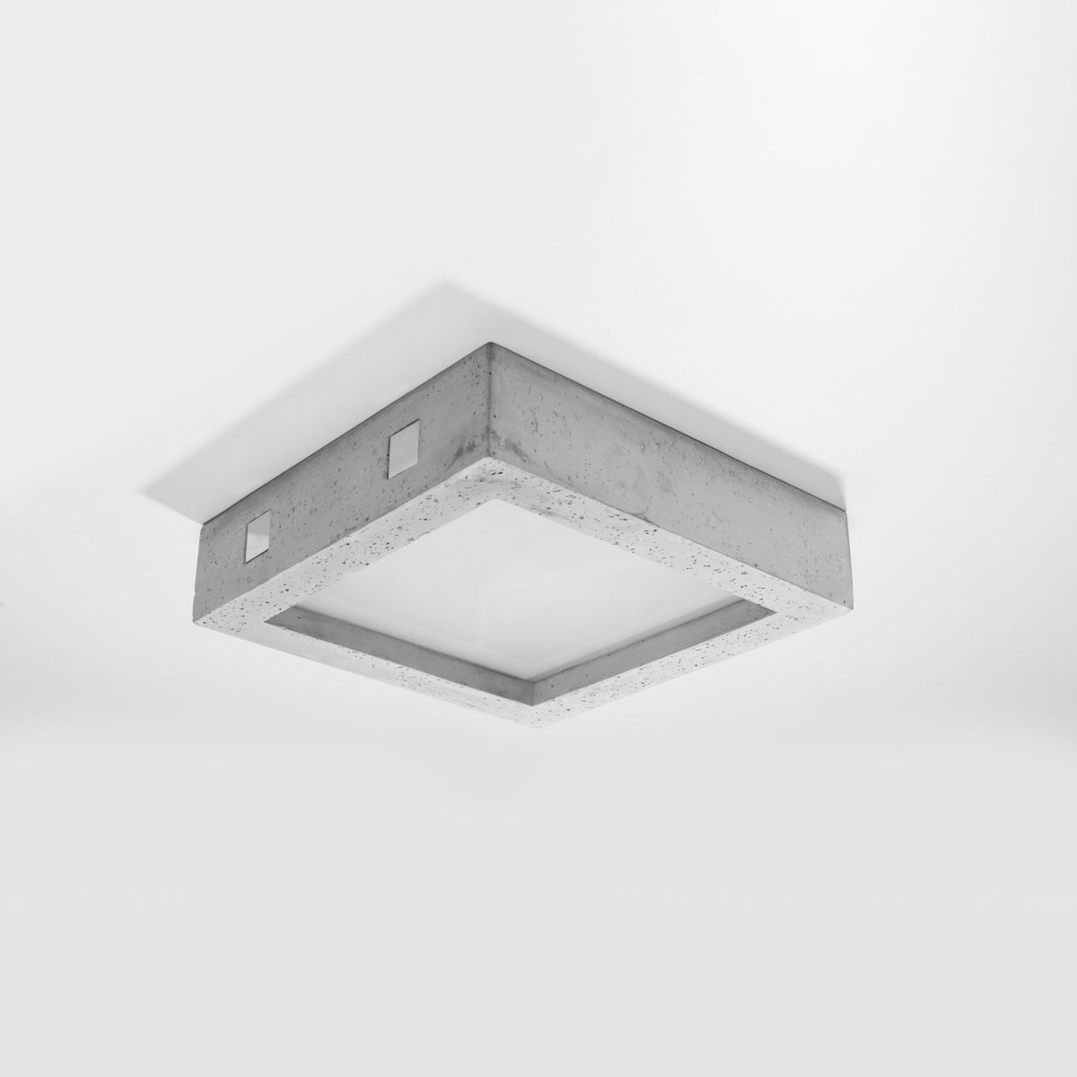 Plafonnier carré en béton installé au plafond blanc, éteint, vu de trois quarts.