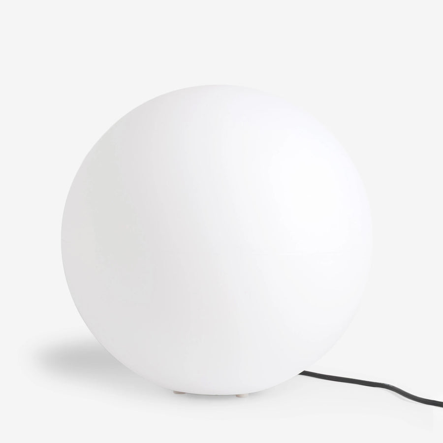 Luminaire sphérique blanc éteint posé au sol, câble noir visible sur fond clair