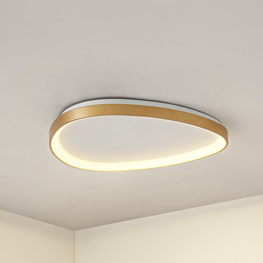 Plafonnier doré ovale allumé, vu de dessous, fixé au plafond d'une pièce vide.