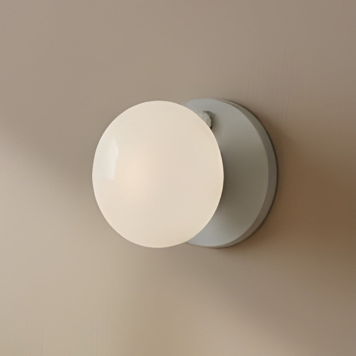 Applique murale ronde en verre opalin blanc et support gris fixée au mur.