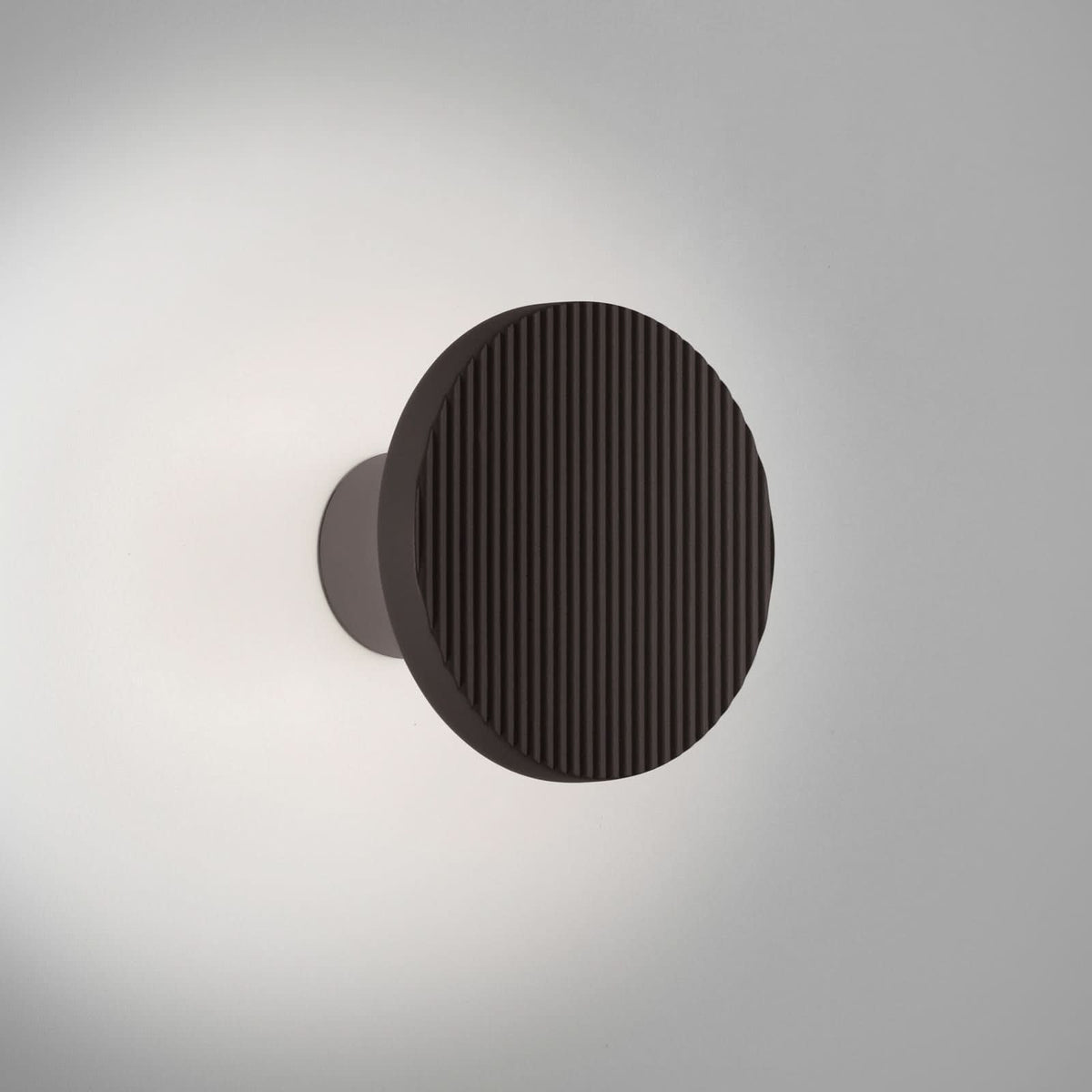 Vue de face de l’applique murale noire, stries verticales et halo lumineux.