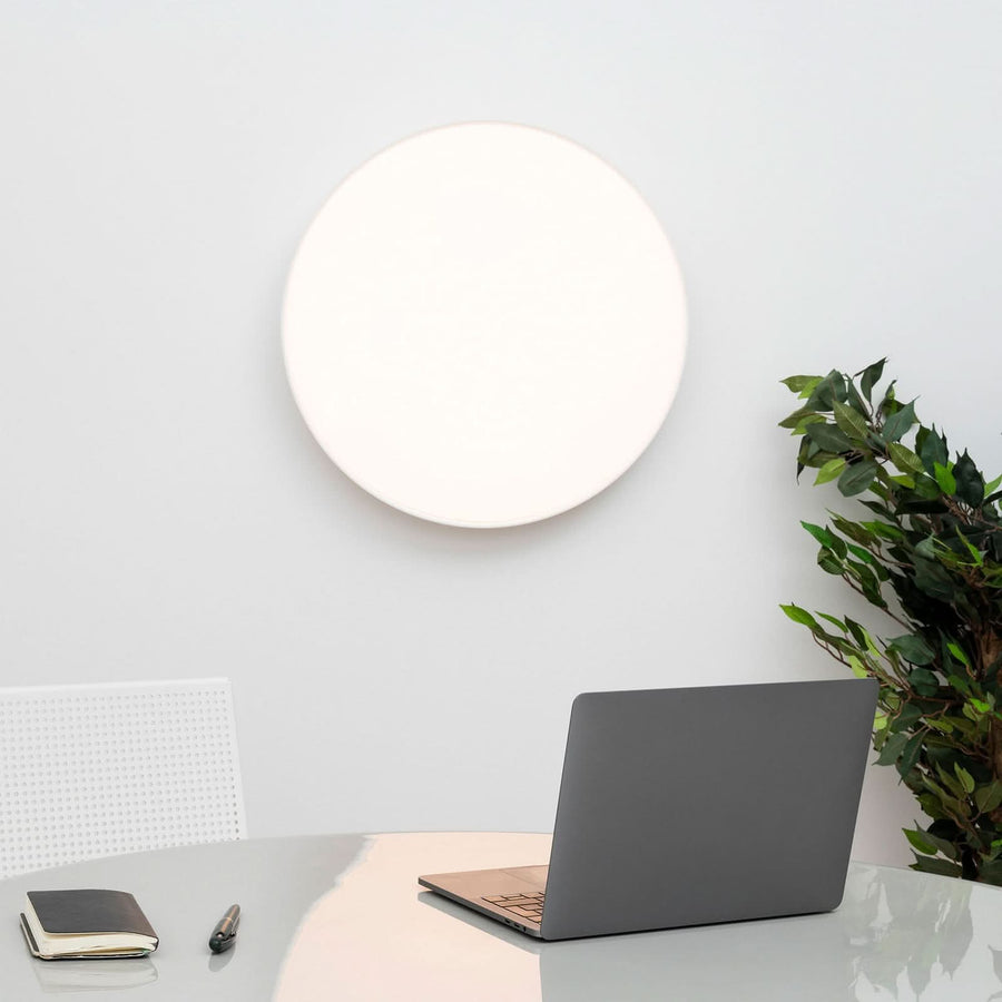 Applique murale ronde blanche allumée au-dessus d'un bureau gris.