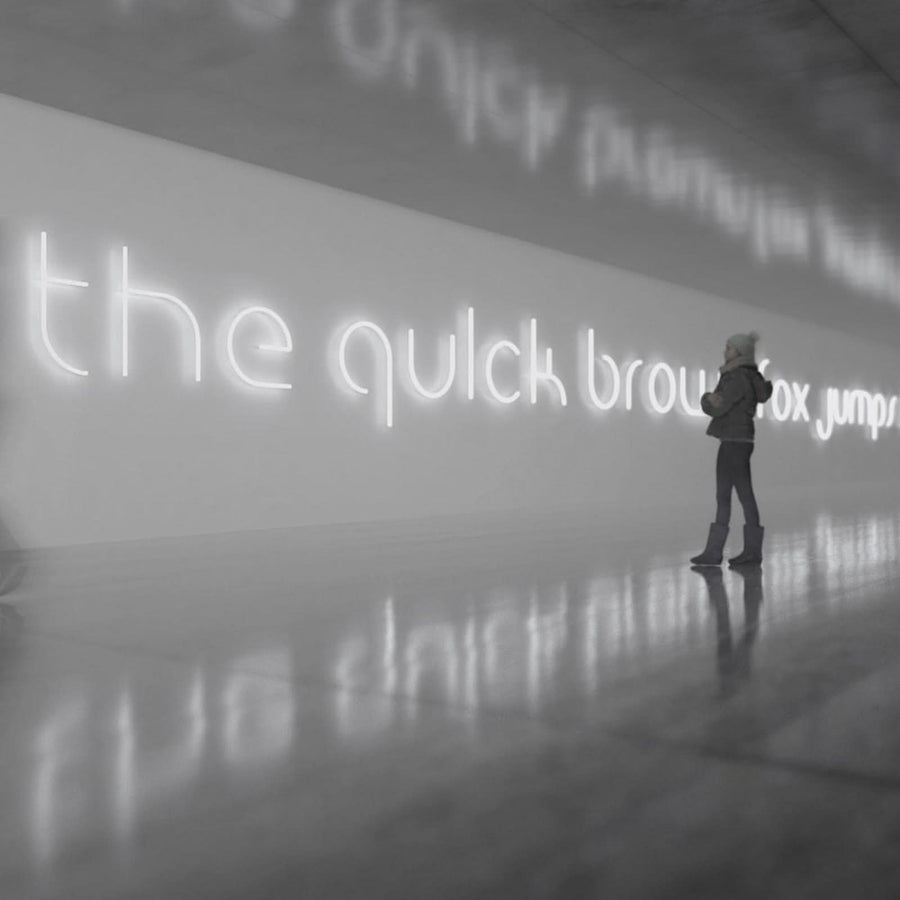 Personne debout devant une longue phrase lumineuse blanche sur mur clair