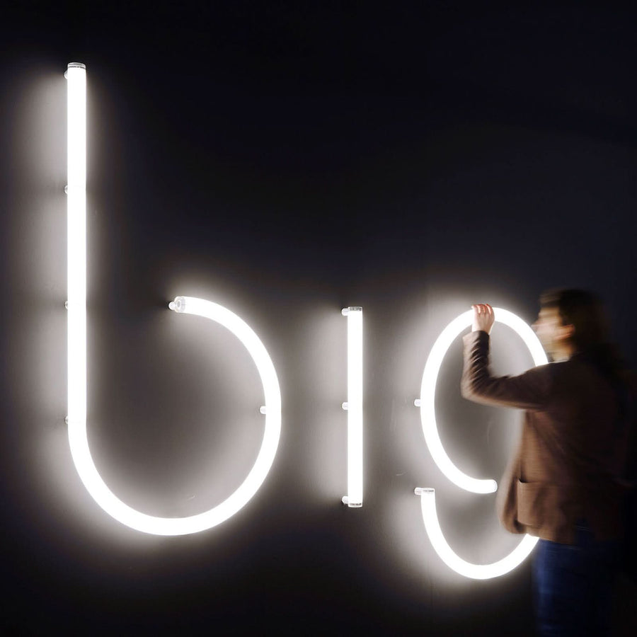 Personne touchant le mot lumineux big en grandes lettres blanches sur mur sombre.