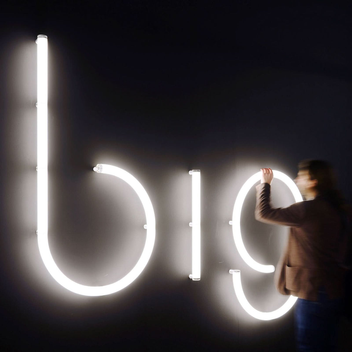 Mise en ambiance nocturne avec une personne ajustant de grandes lettres lumineuses blanches au mur.