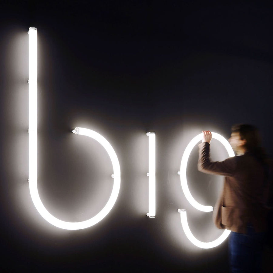 Personne ajustant de grandes lettres lumineuses blanches sur un mur sombre.