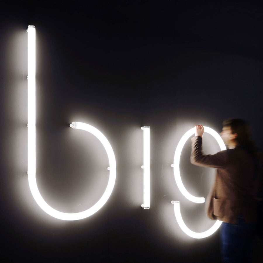 Une personne ajuste de grandes lettres lumineuses blanches sur un mur sombre