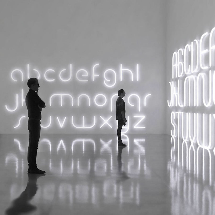 Deux silhouettes contemplent un mur couvert de lettres lumineuses blanches