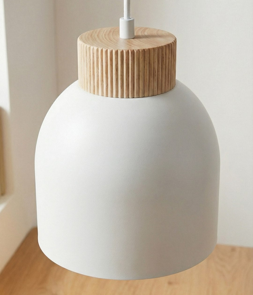 Gros plan sur un abat-jour blanc et sa couronne en bois rainuré, câble blanc.