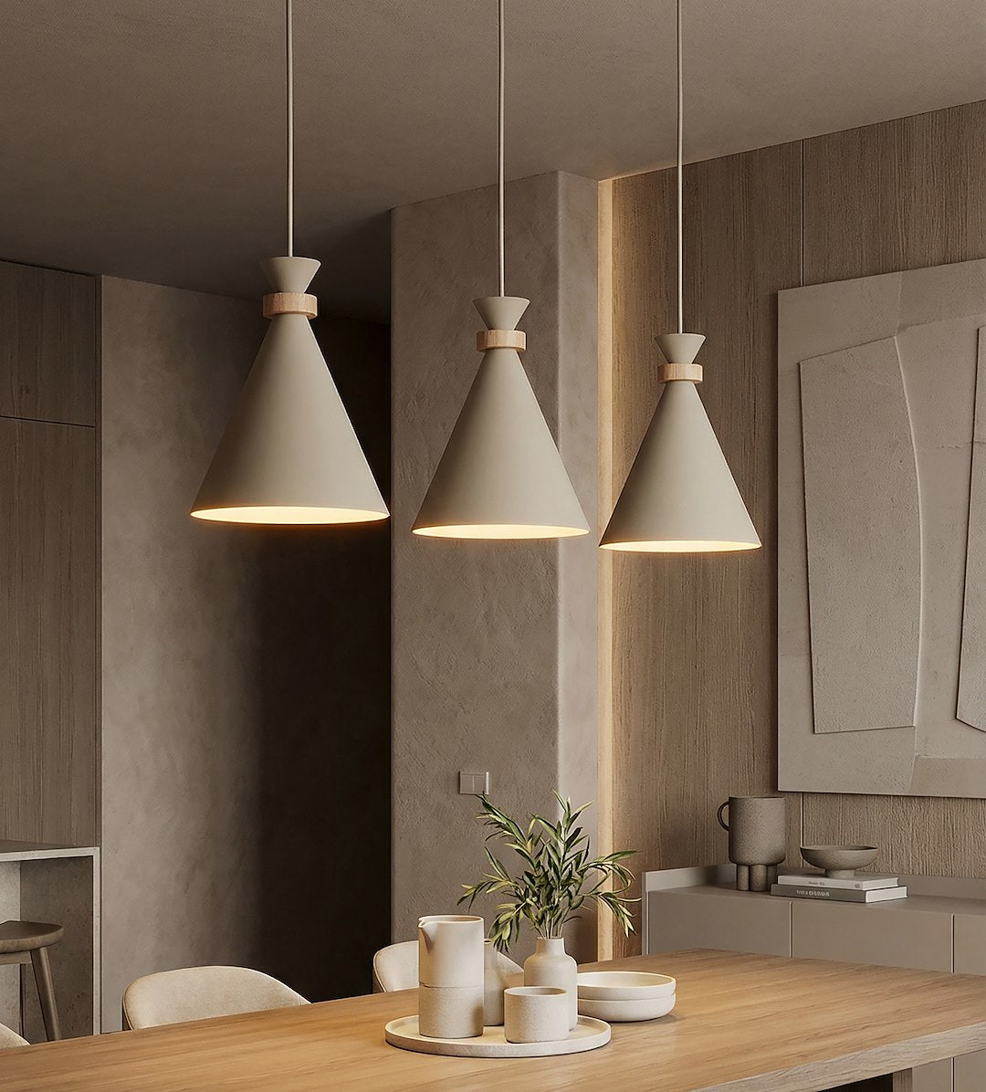 Mise en ambiance cuisine, trois suspensions allumées au-dessus d'une table en bois et d'une nature morte