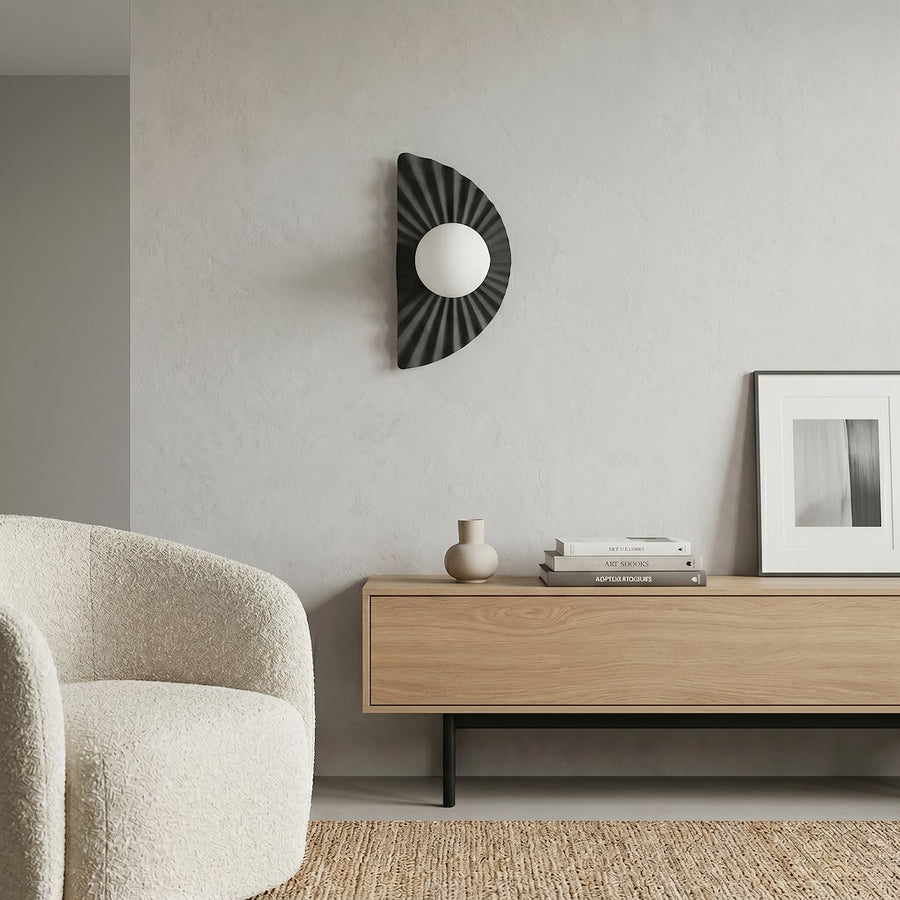 En situation dans un salon : applique murale sur mur clair, fauteuil bouclé et meuble.