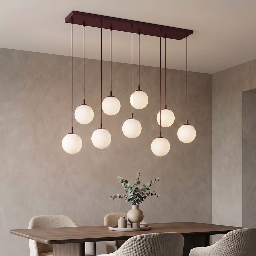 Suspension allumée éclairant une salle à manger beige, table en bois et vase d'eucalyptus