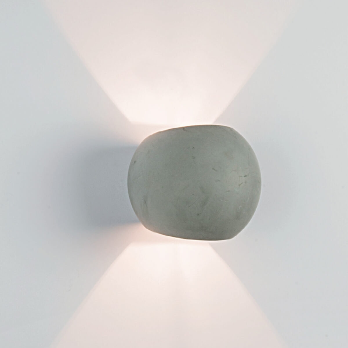 Vue rapprochée du luminaire mural en béton brut et de ses faisceaux lumineux