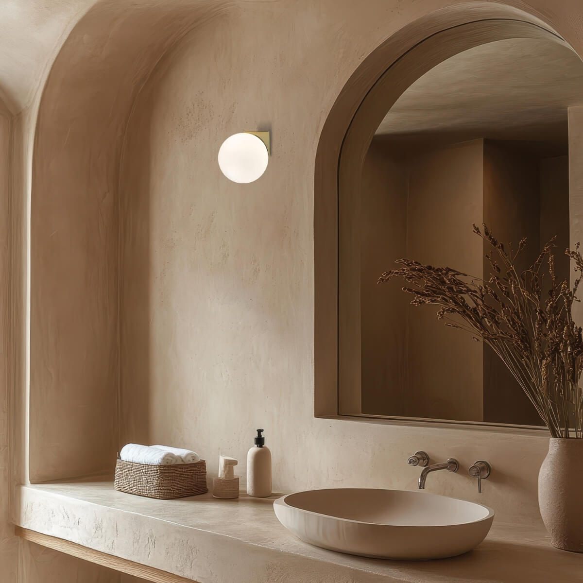 Ambiance intérieure beige, applique globe allumée près d'un miroir cintré et vasque en pierre.