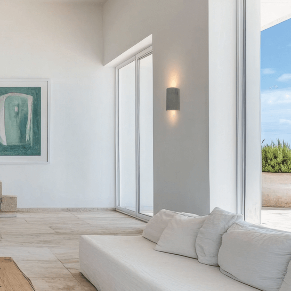 Vue rapprochée du salon : applique béton allumée sur un mur blanc proche des fenêtres