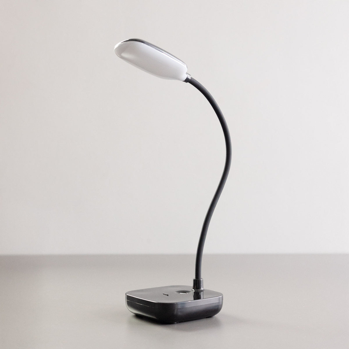 Lampe noire éteinte de trois quarts sur fond blanc, tête ovale et col flexible.