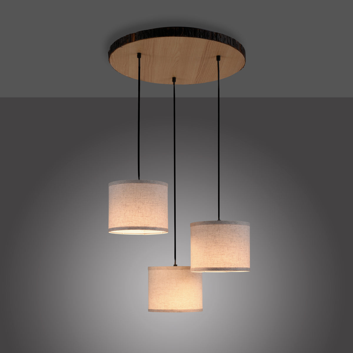 Luminaire allumé dans la pénombre, halo chaud diffusé par les trois abat-jours cylindriques.