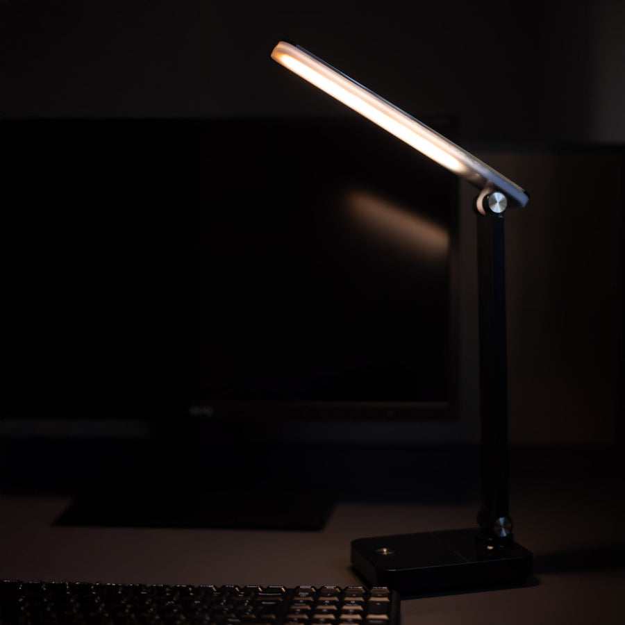 Lampe de bureau allumée près d'un clavier et d'un écran d'ordinateur dans le noir.