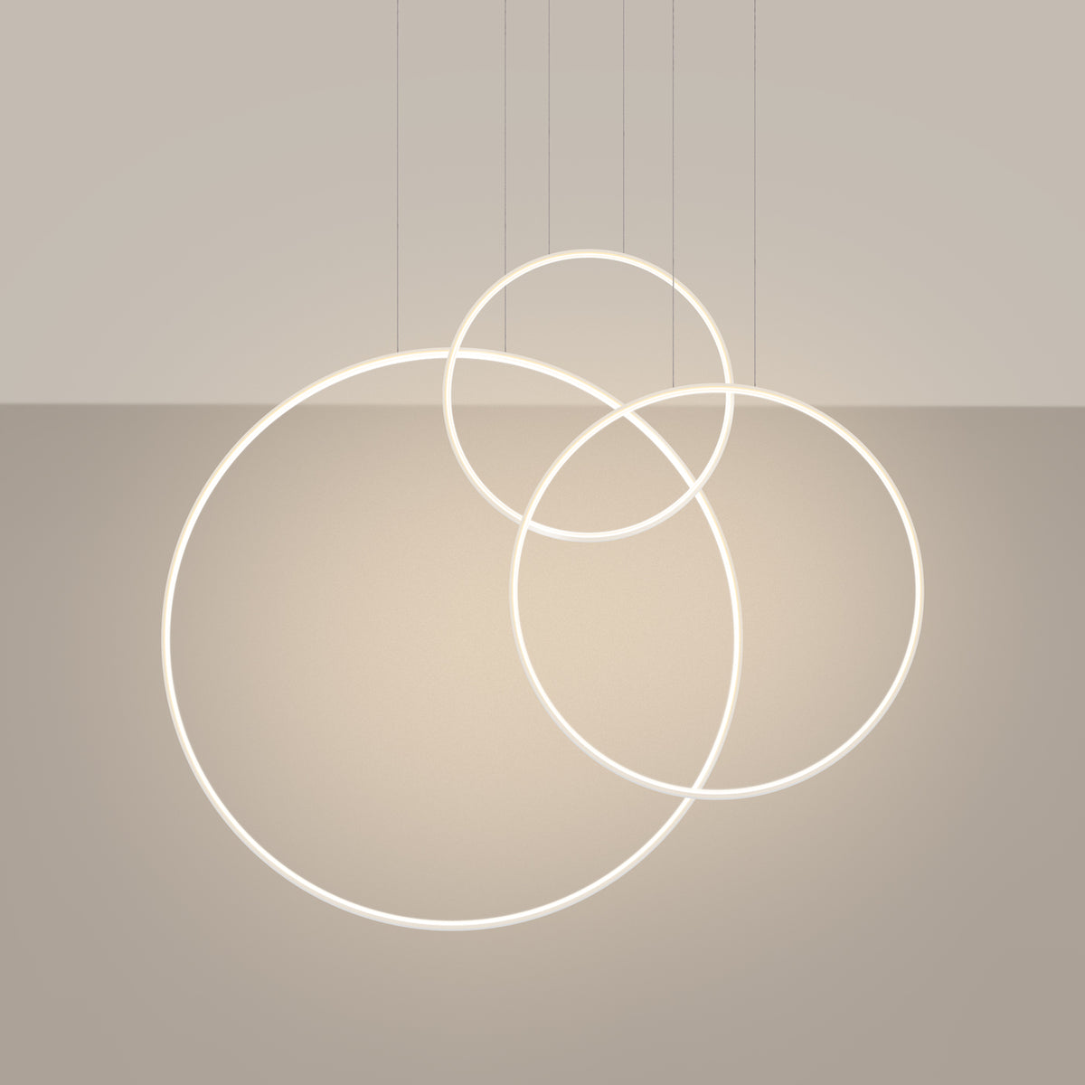Luminaire allumé en ambiance, trois anneaux lumineux se croisant sur fond beige