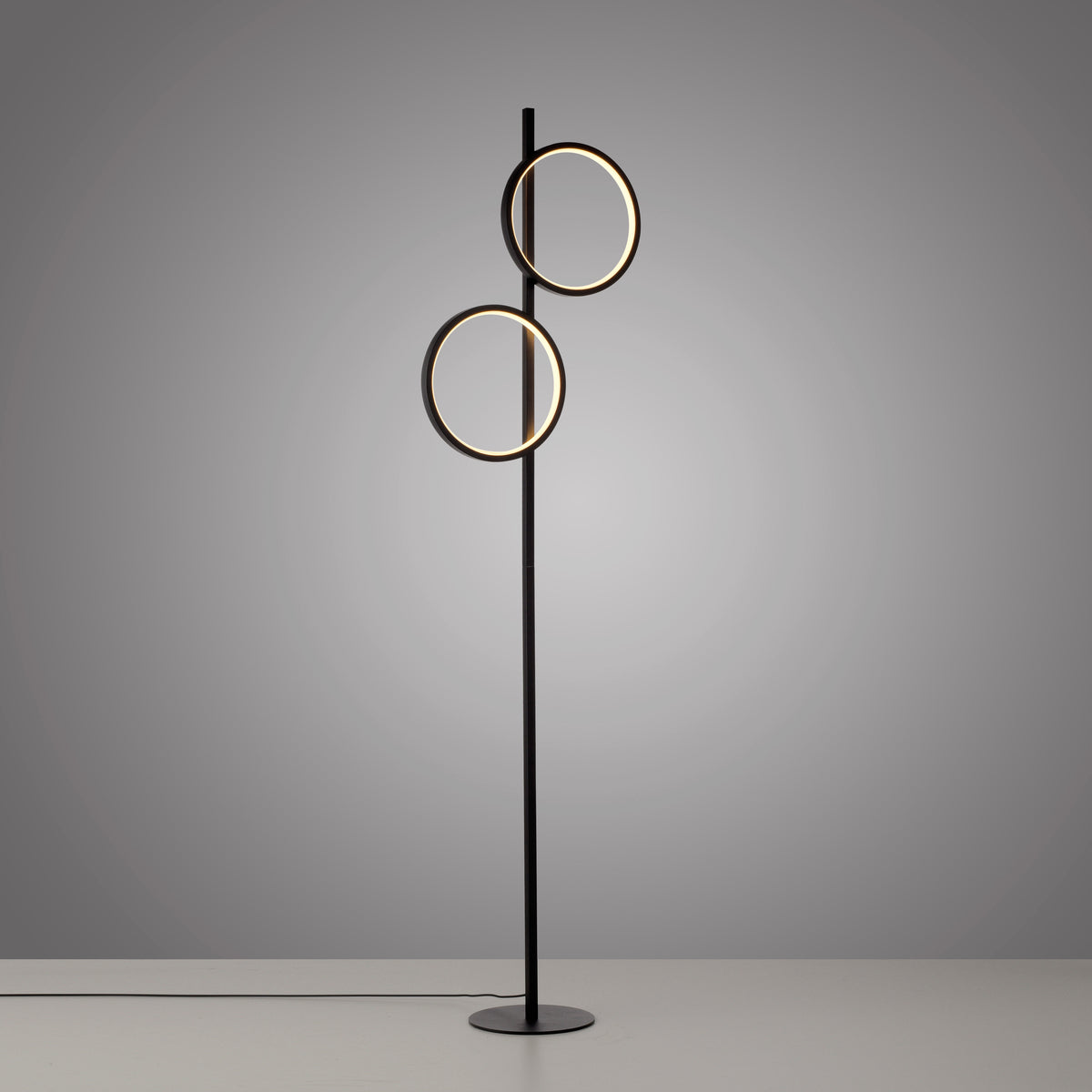Lampadaire noir allumé, câble au sol, deux anneaux lumineux sur fond gris.