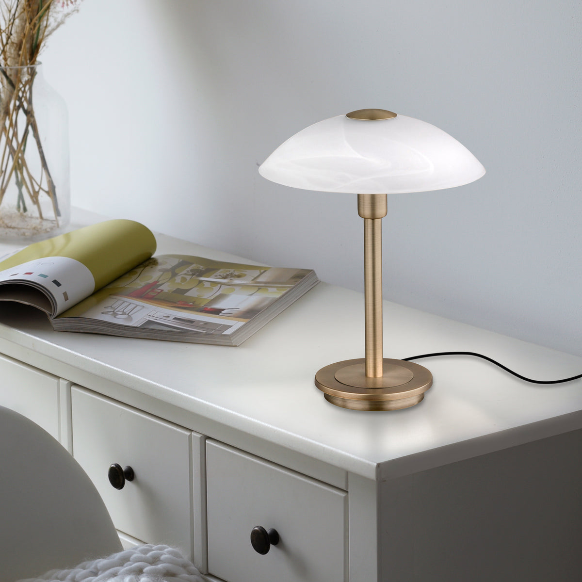 Mise en ambiance sur une commode blanche, lampe allumée près d'un magazine