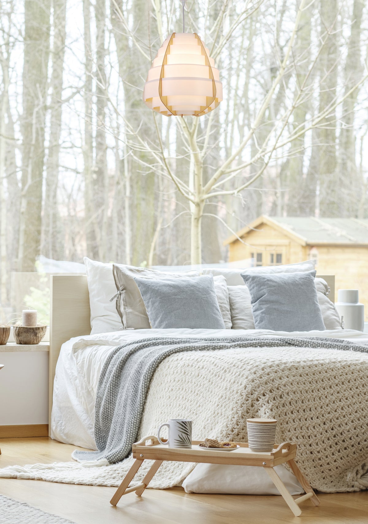 Luminaire suspendu dans une chambre claire, devant une fenêtre ouvrant sur la forêt