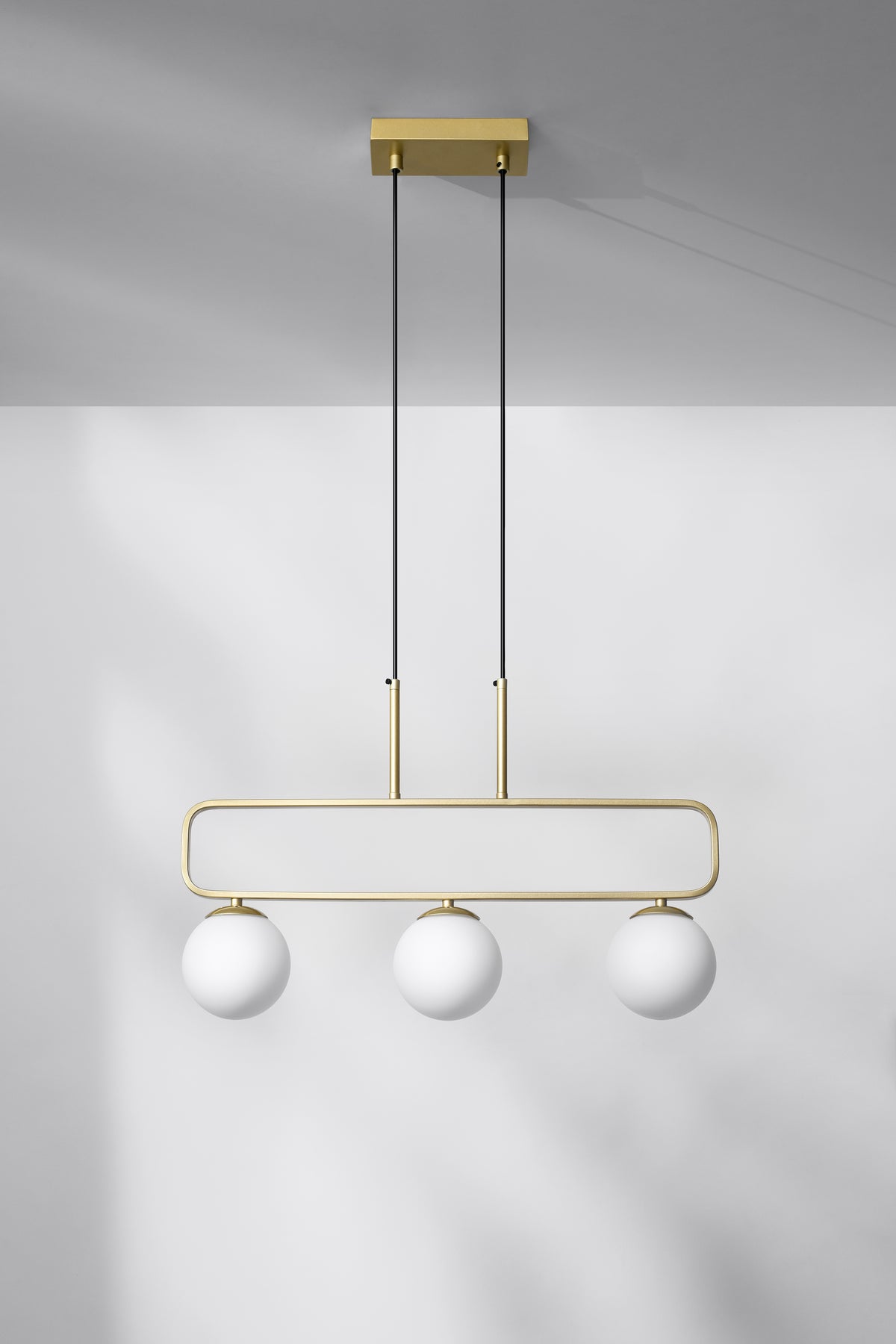 Luminaire suspendu devant un mur clair, jeu d'ombres douces
