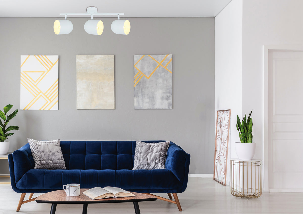 Mise en ambiance dans un salon, plafonnier blanc orienté vers un mur gris et canapé bleu
