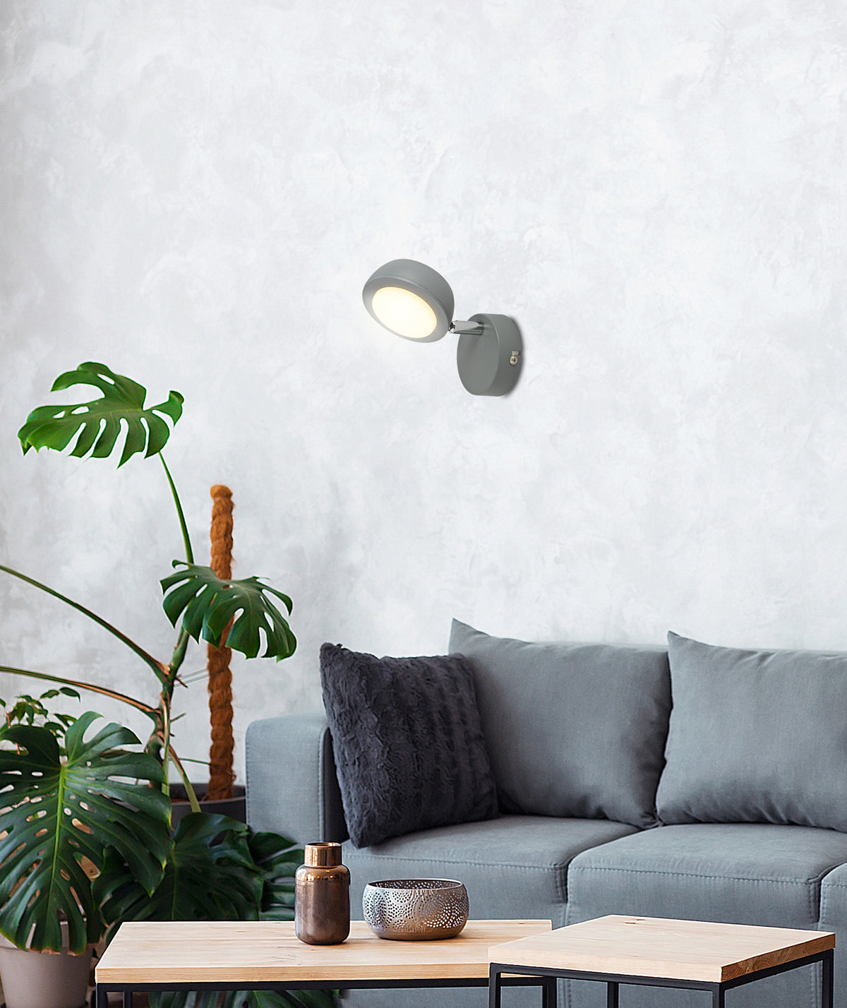 Mise en ambiance du salon : applique grise allumée au-dessus d'un canapé et d'un monstera