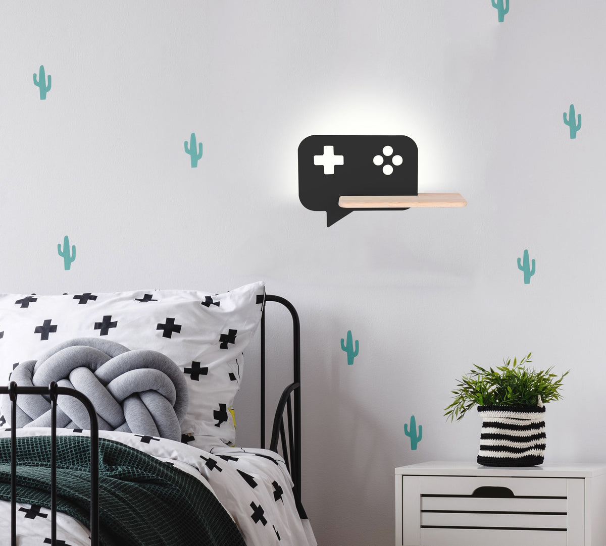 Applique murale allumée au-dessus d'un lit, décor de cactus et chevet blanc
