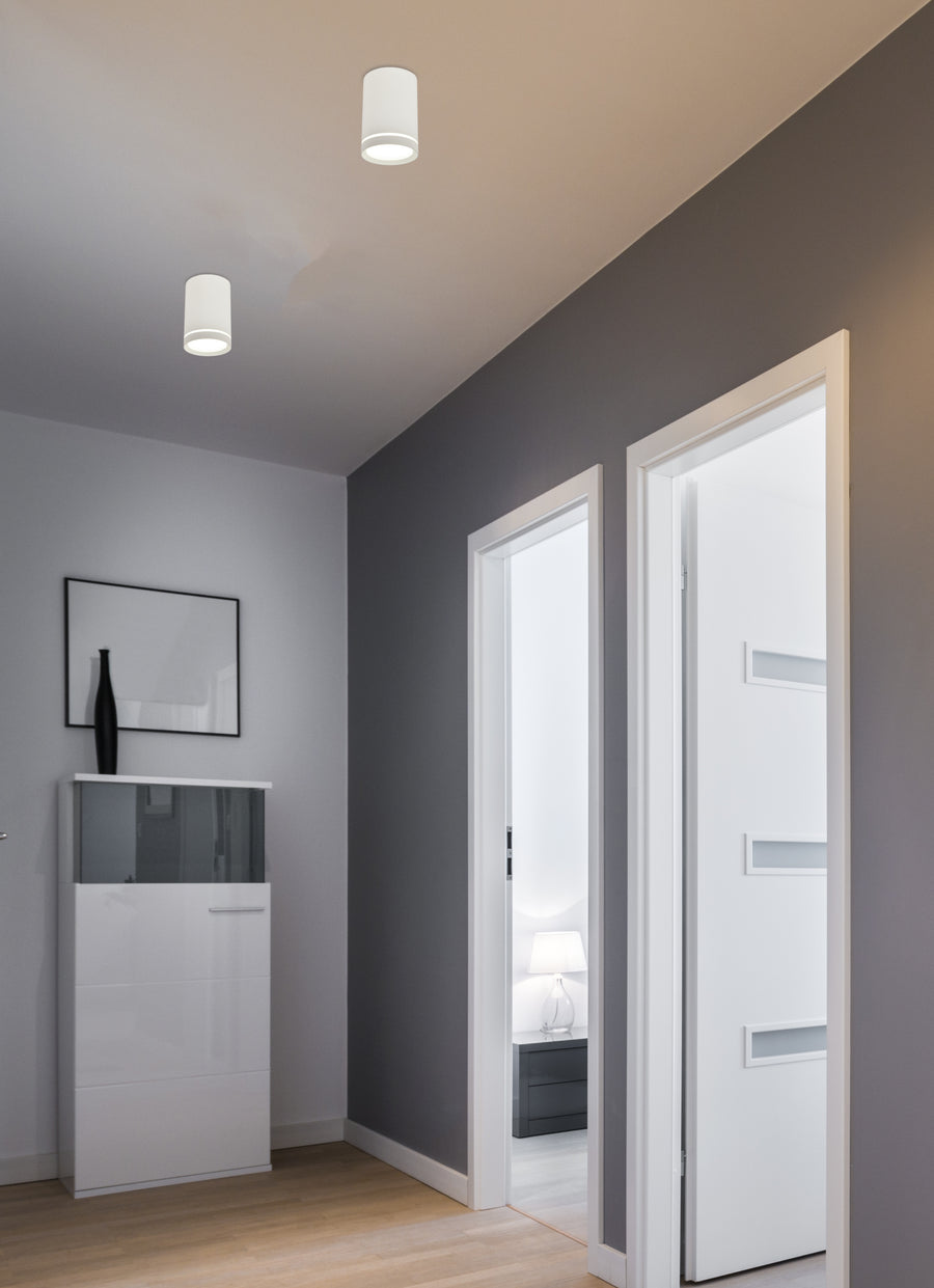 Deux plafonniers cylindriques blancs allumés au plafond d'un couloir gris contemporain