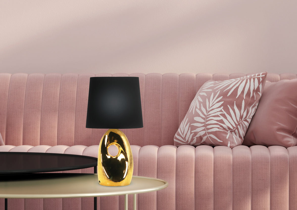 Ambiance salon rose, lampe dorée à abat-jour noir posée sur table basse