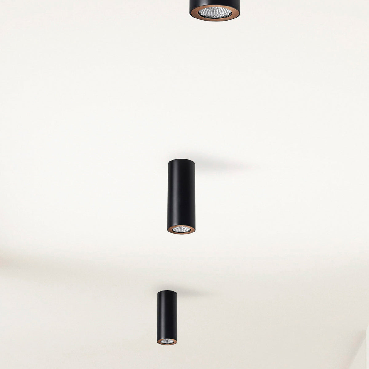 Trois spots cylindriques noirs fixés au plafond, vus en perspective