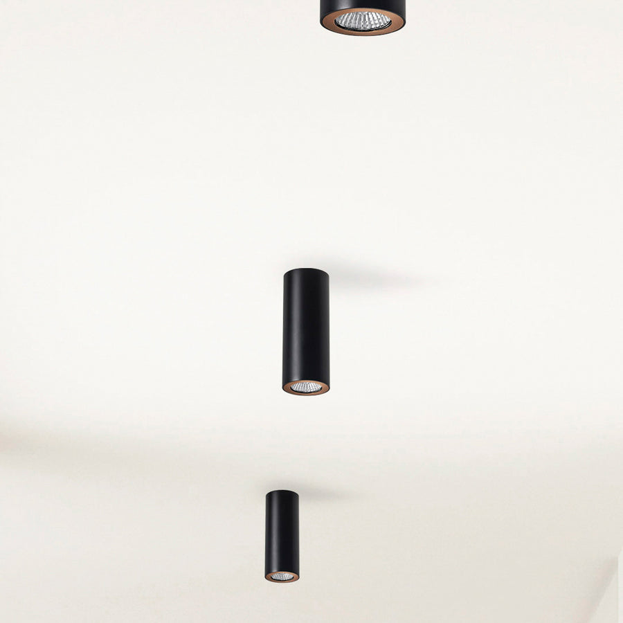 Trois spots cylindriques noirs fixés au plafond, vus en perspective