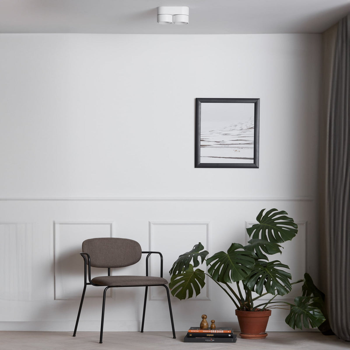 Luminaire blanc fixé au plafond dans un salon minimaliste, avec chaise et plante.