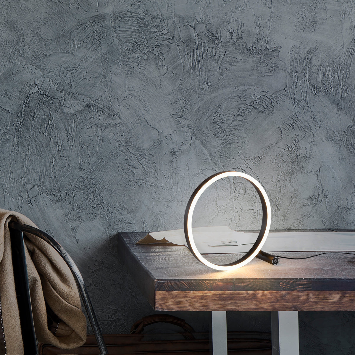 Mise en ambiance : lampe posée sur table en bois devant mur béton gris