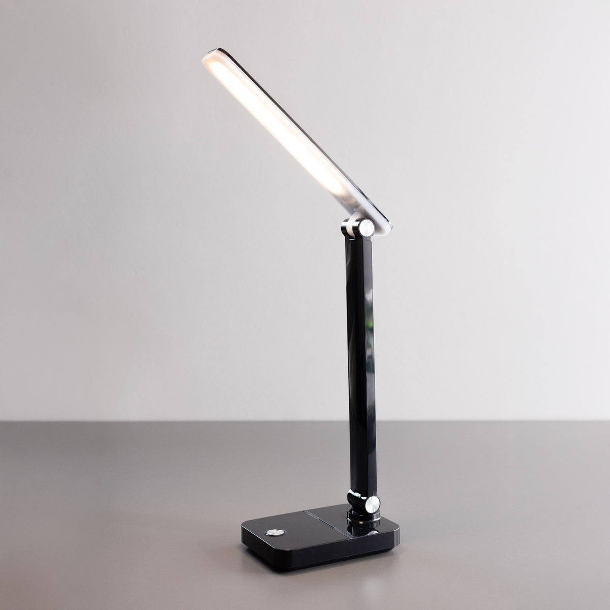 Vue de trois-quarts d'une lampe de bureau noire allumée, orientée vers le haut.
