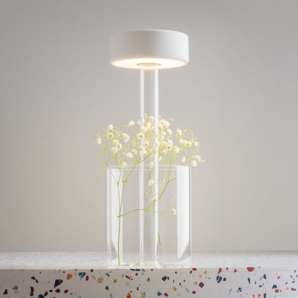 Lampe dont le socle en verre sert de vase avec des fleurs blanches