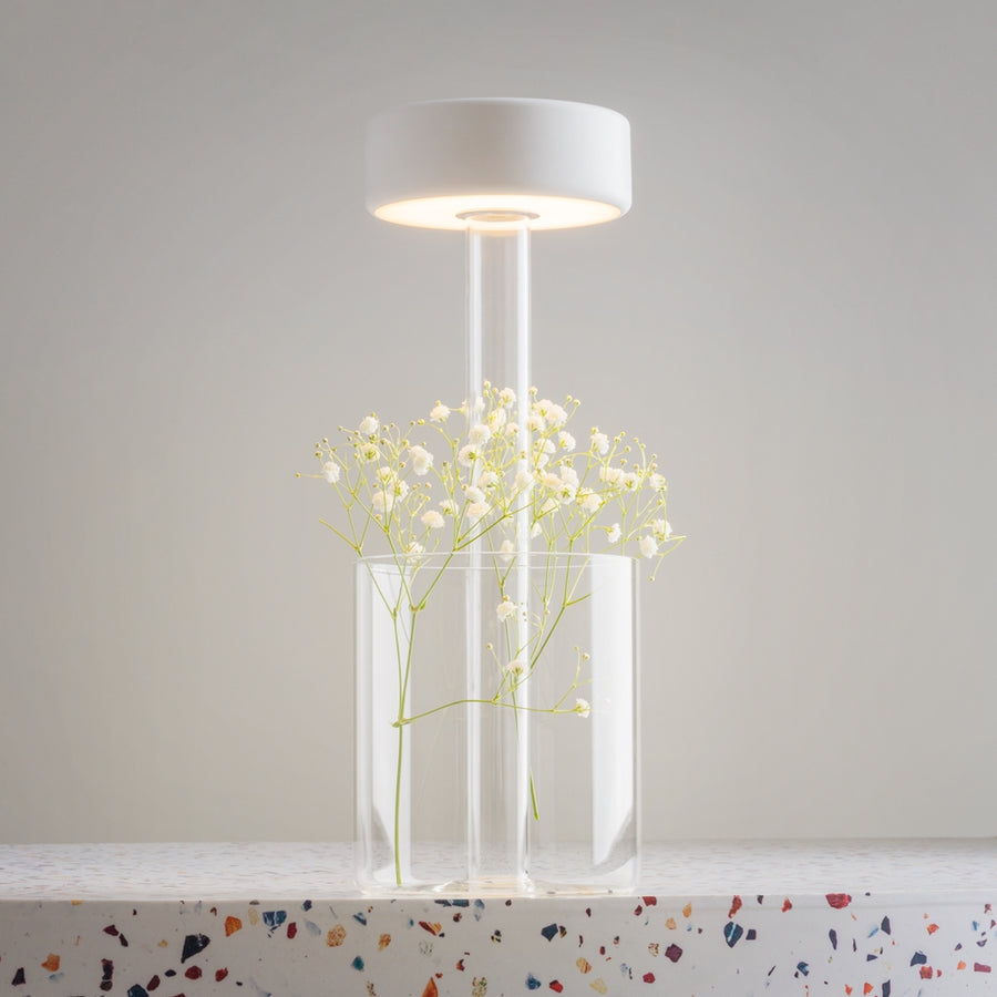 Lampe dont le socle en verre sert de vase avec des fleurs blanches