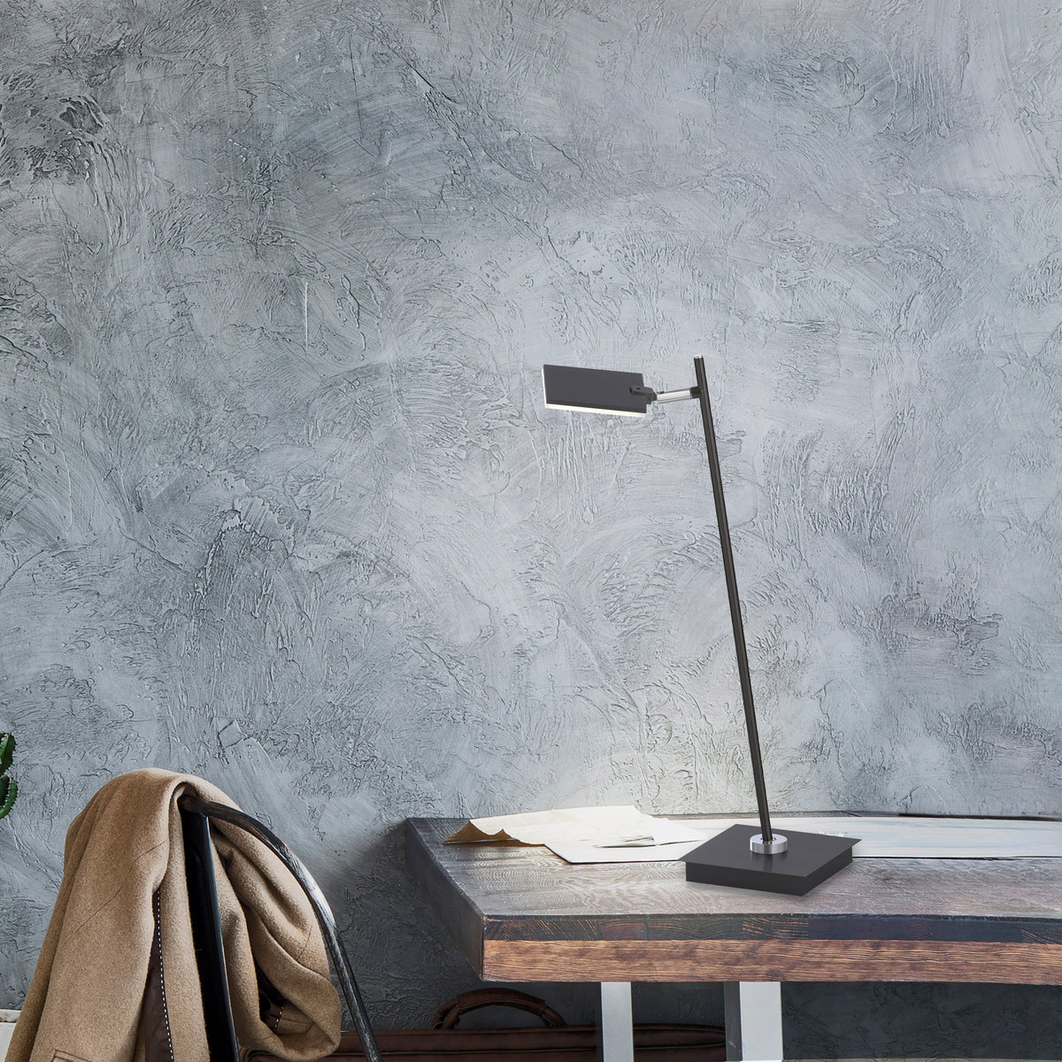 Mise en ambiance sur un bureau en bois devant un mur gris texturé, avec chaise.