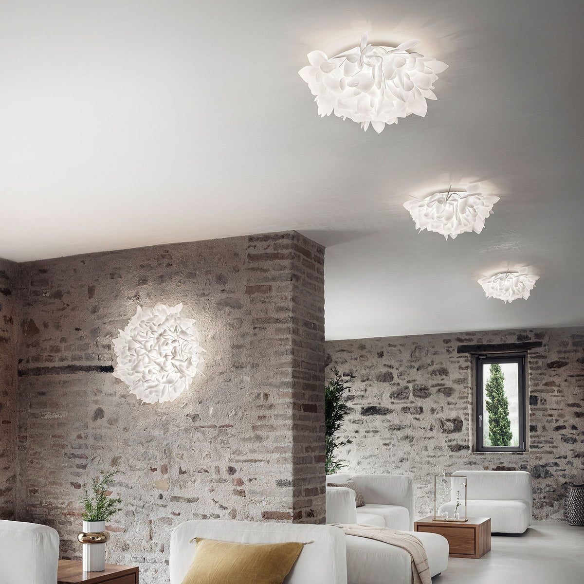 Mise en ambiance dans un salon en pierre, applique murale et plafonniers blancs allumés.