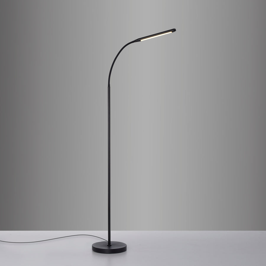 Lampadaire posé sur une table blanche, câble visible, lumière allumée.