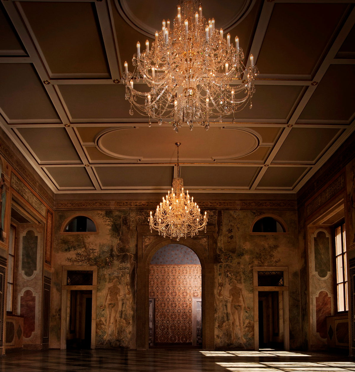 Grande salle décorée avec lustres en cristal suspendus, plafond à caissons et fresques murales.