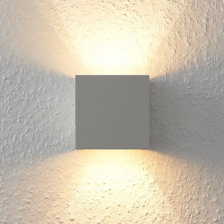 Vue de face de l'applique carrée blanche allumée sur un mur texturé.
